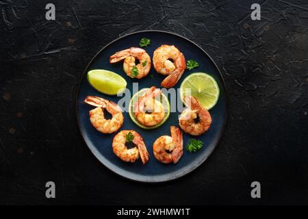 Shrimps, oben flach auf Schwarz geschossen. Gekochte Garnelen mit Limette Stockfoto
