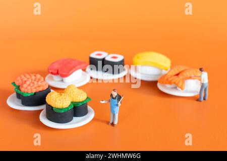 Winziger Koch, der Sushi auf orangefarbenem Hintergrund zubereitet Stockfoto
