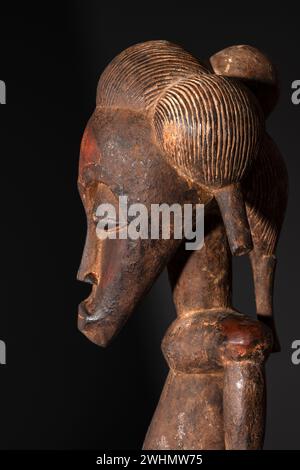 Nahaufnahme einer hölzernen Senufo männlichen Figur aus der Elfenbeinküste mit brauner Patina isoliert auf Schwarz. Afrikanische Stammeskunst mit meisterhafter Handwerkskunst A Stockfoto