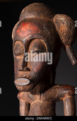 Nahaufnahme einer hölzernen Senufo männlichen Figur aus der Elfenbeinküste mit brauner Patina isoliert auf Schwarz. Afrikanische Stammeskunst mit meisterhafter Handwerkskunst A Stockfoto