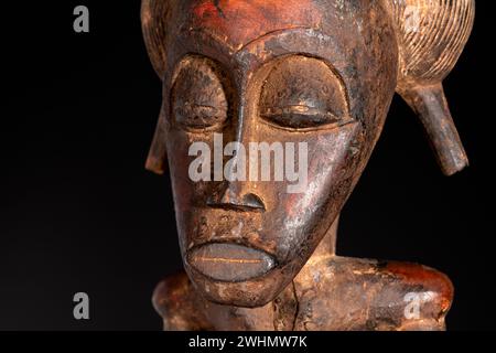 Nahaufnahme einer hölzernen Senufo männlichen Figur aus der Elfenbeinküste mit brauner Patina isoliert auf Schwarz. Afrikanische Stammeskunst mit meisterhafter Handwerkskunst A Stockfoto