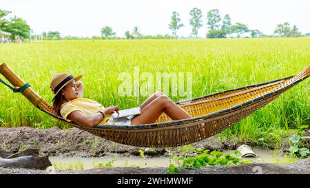 Asiatische Frauen in der Hängematte arbeiten an einem Laptop mit grünen Reisfeldern im Hintergrund Stockfoto