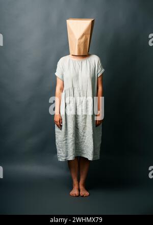Ganzes Porträt einer Frau im langen Kleid, die sich unter leerem Papierbeutel versteckt Stockfoto