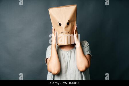 Verärgerte Frau mit einer Papiertüte auf dem Kopf, die Schläfen berührt, unter starken Spannungskopfschmerzen Stockfoto