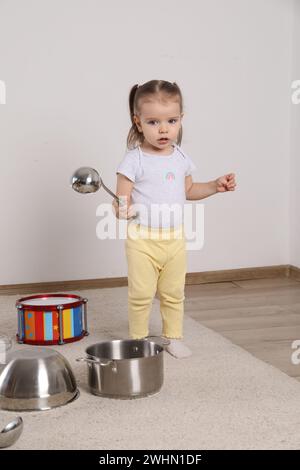 Niedliches kleines Mädchen mit Kochgeschirr und Spielzeugtrommel zu Hause Stockfoto