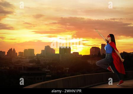 Superheld, Motivation und Kraft. Frau in cape und Maske auf hohem Gebäude in der Stadt Stockfoto