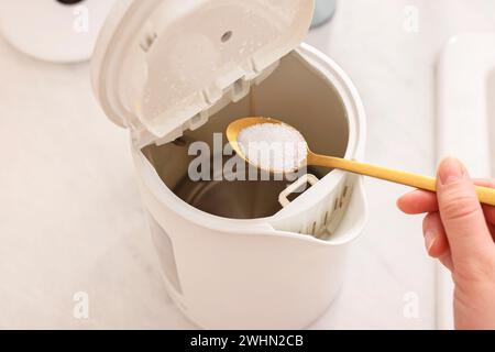 Reinigen des elektrischen Wasserkochers. Frau, die Backpulver in das Gerät am Tisch einfüllte, über der Ansicht Stockfoto