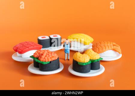 Winziger Koch, der Sushi auf orangefarbenem Hintergrund zubereitet Stockfoto