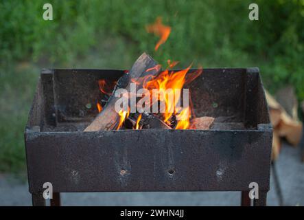 Rustikaler Barbecue-Grill aus Metall im Freien mit Brennholz. Feuerflamme zum Grillen beim Sommerpicknick im grünen Garten. Stockfoto