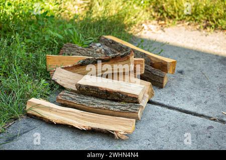 Holzstücke für Brennholz, die im Sommer auf einem grünen Hinterhof gestapelt werden und zum Grillen oder Grillen beim Picknick verwendet werden. Stockfoto