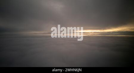 Helle Sonnenstrahlen Licht scheint über dunklem bewölktem Himmel. Sonnenuntergang aus dem Flugzeug Stockfoto