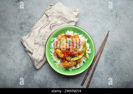 Asiatisches süß-saures Hähnchen mit Gemüse, gebraten und Reis in einer Keramikschale mit Stäbchen von oben, grauer rustikaler ston Stockfoto