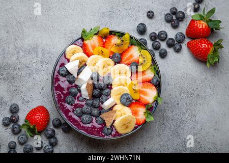 Gesunde Sommer Acai Smoothie Schüssel mit Chiasamen, frische Banane, Erdbeere, Heidelbeere, kokos, kiwi-Draufsicht, rustikaler Betonboden Stockfoto