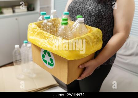 Recyceln Sie die umweltfreundliche Zero Concept Frau, die leere Plastikflasche mit gelben Mülltüten zu Hause in den Recyclingbehälter wirft. Stockfoto