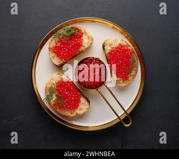 Sandwiches mit rotem Kaviar und Brot auf einem runden Teller auf einem schwarzen Tisch, Blick von oben Stockfoto