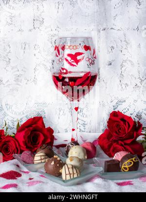 Romantische Rosen, Wein und Pralinen befinden sich in einem Stillleben mit Spitzenvorhang Hintergrund Stockfoto