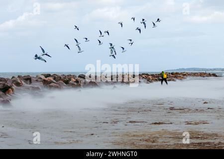 Wellenbrecher, Steine und ein Mann, der in einem windigen Sandsturm am Strand spaziert. Wildes Surfen mit Wellen Stockfoto