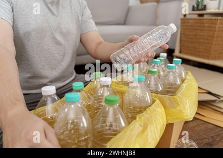 Recyceln Sie den umweltfreundlichen Zero Concept-Mann, der leere Plastikflasche in den Recyclingbehälter mit gelben Mülltüten zu Hause wirft Stockfoto