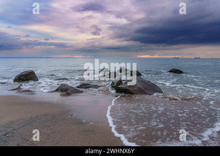 Felsen verstreut am Sandstrand mit Blick auf das Meer an bewölkten Tagen Stockfoto