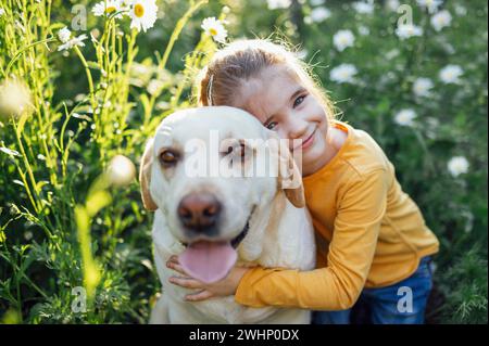 Süßes kleines Mädchen, das ihren Hund umarmt - goldener labrador Retriever. Stockfoto