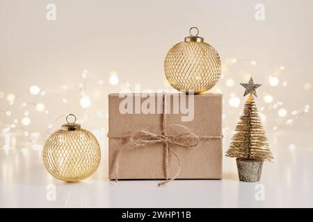 Nachhaltige Geschenkboxen mit goldenen Kugeln und Weihnachtsbaum auf glänzendem Bokeh-Hintergrund Stockfoto