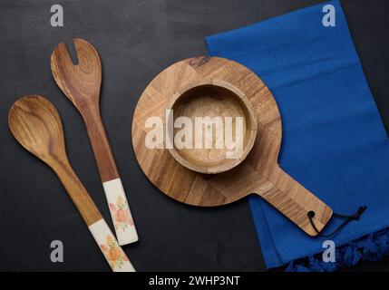 Leere Schüssel und Holzlöffel auf einem schwarzen Tisch, Blick von oben Stockfoto