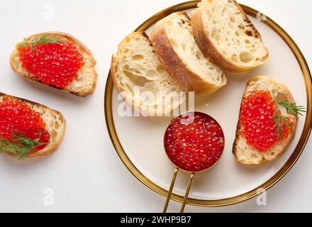 Sandwiches mit rotem Kaviar und Brot auf einem runden Teller auf einem weißen Tisch, Blick von oben Stockfoto