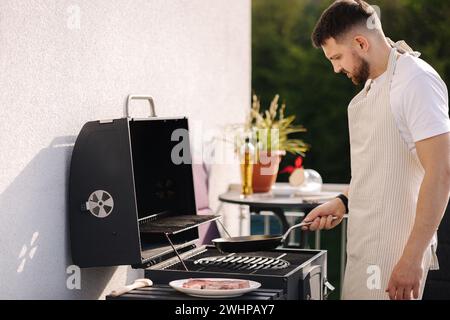 Mittlere Auswahl eines Mannes in der Schürze mit einem Holzlöffel zum Mischen von Gemüse in der Bratpfanne. Bereiten Sie Speisen auf dem Grill zu Stockfoto