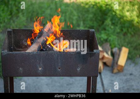 Rustikaler Barbecue-Grill aus Metall im Freien mit Brennholz. Feuerflamme zum Grillen beim Sommerpicknick im grünen Garten. Stockfoto