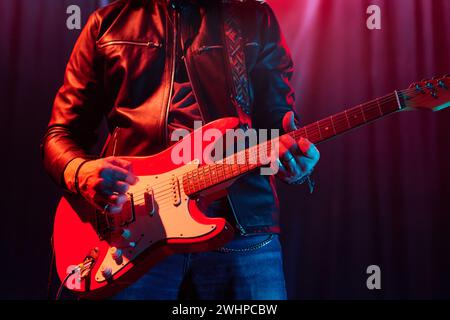 Zugeschnittene Aufnahme eines nicht erkennbaren Rockmusikers, der elektrische Gitarre auf der Bühne spielt und einen Kopierraum in Lederjacke trägt Stockfoto