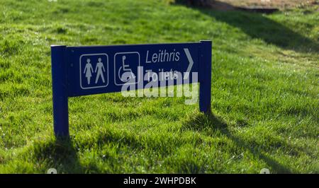 Blaues Schild auf dem grünen Gras, das die Richtung für Toiletten anzeigt Stockfoto