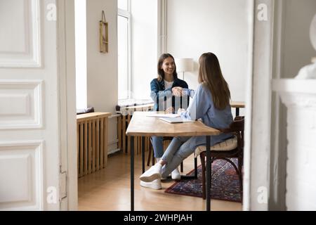 Positive Millennials-Geschäftspartnerinnen in Freizeitkleidung, die sich die Hände schütteln Stockfoto