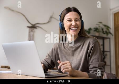 Fröhliche freiberufliche Angestellte Frau in kabellosen Kopfhörern, die am Laptop sitzt Stockfoto