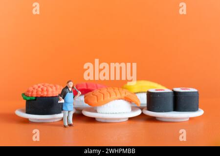 Winziger Koch, der Sushi auf orangefarbenem Hintergrund zubereitet Stockfoto