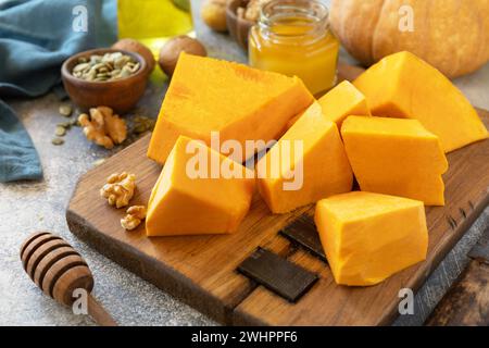 Roher Kürbis, Honig, Kürbiskerne und Nüsse auf grauem Steingrund. Stockfoto