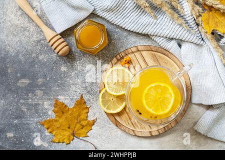 Heißer Kräuter-Vitamin-Sanddorn-Tee in einer Glasschale mit frischen Sanddorn-Beeren, Honig und Zitrone auf einer Steinplatte. Entspannen Sie Sich Stockfoto
