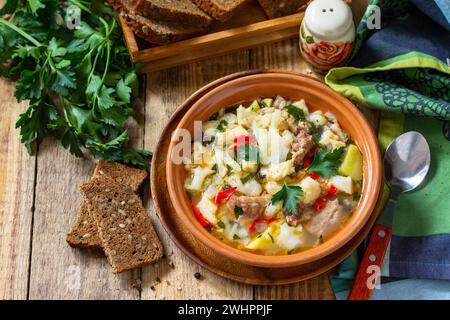 Traditionelle ungarische dicke Suppe mit Rindfleisch, Gemüse und Knödeln auf einem Holztisch. Warmes Abendessen oder Mittagessen. Stockfoto