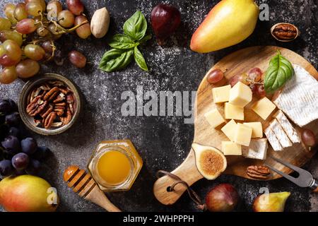 Käseplatte, Stillleben von saisonalen Wein-Snacks. Brie-Käse, frische Feigen, Trauben, Käsewürfel, Birnen, Pekannüsse und Honig drauf Stockfoto