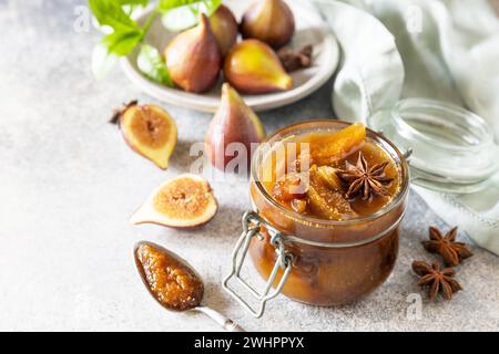 Hausgemachte süße Feigen-Marmelade in einem Glasgefäß mit frischen Feigen auf einem hellgrauen Tisch. Herbsternterhaltung, gesunde fermentierte Nahrung Stockfoto