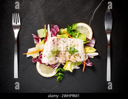 Gegrilltes Kabeljaufilet mit Salat auf schwarzem Schieferteller Stockfoto