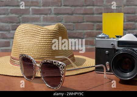 Eine alte Kamera mit Sonnenbrille und Strohhut mit Krempe. Stillleben Stockfoto