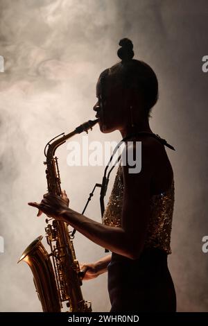 Seitenansicht einer schwarzen Frau, die Saxophon spielt und Jazz-Musik mit Rauch spielt Stockfoto