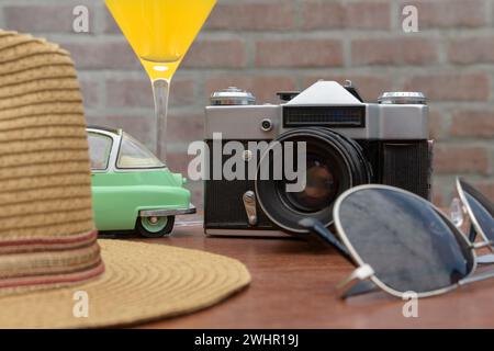 Orangefarbener Cocktail, alte Kamera, Sonnenbrille und Strohhut mit Krempe auf Holztisch Stockfoto