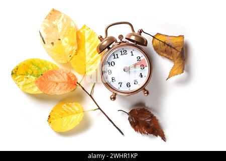 Im Herbst nach Sommerzeit auf einem Vintage-Wecker und einigen farbigen Blättern auf weißem Hintergrund, Stockfoto