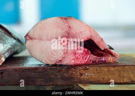 Frischer Thunfisch, der zur Hälfte auf Holzbrett geschnitten wurde, kann auf dem Muscat Fish Market verkauft werden. Makroaufnahme in Nahaufnahme mit Details zur Fleischstruktur Stockfoto