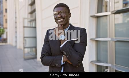 Selbstbewusster afroamerikanischer Mann in einem stilvollen Anzug posiert auf einer Stadtstraße mit einem fröhlichen Lächeln. Stockfoto