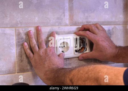 Das Bild zeigt die Hände eines Elektrikers, der die in die Wand eingebauten Steckdosen repariert. Stockfoto