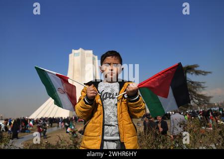 Teheran, Iran. Februar 2024. Ein iranischer Junge weht iranische und palästinensische Flaggen auf dem Azadi-Platz, während er sich zum 45. Jahrestag der Islamischen Revolution in Teheran versammelte. Der Iran bezeichnete am 11. Februar 2024 den 45. Jahrestag der Islamischen Revolution von 1979, inmitten von Spannungen, die den Nahen Osten über den fortgesetzten Krieg Israels gegen die Hamas im Gazastreifen ergriffen haben. Der iranische Präsident Ebrahim Raisi verurteilte den Erzfeind Israel und verlangte seine Ausweisung aus den Vereinten Nationen. (Kreditbild: © Rouzbeh Fouladi/ZUMA Press Wire) NUR REDAKTIONELLE VERWENDUNG! Nicht für kommerzielle ZWECKE! Stockfoto