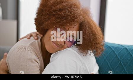 Wunderschönes Paar, Mann und Frau, sich selbstbewusst umarmen und lachen, während sie auf ihrer gemütlichen Couch zu Hause sitzen, ihre Liebe und ihr Glück wundert sich Stockfoto