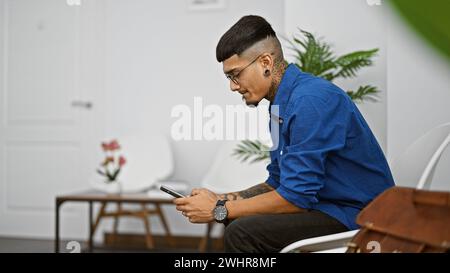 Hübscher junger lateinmann, der in einem geschäftigen Raum sitzt und auf seine Reihe wartet, ein Porträt eines entspannten Profis Stockfoto